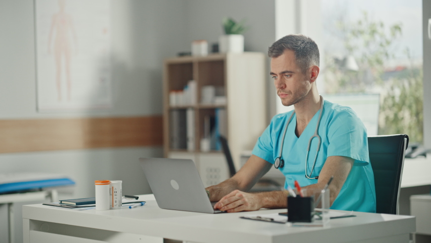 Experienced Male Nurse Wearing Blue Uniform Answering Video Call on Laptop at Doctor's Office. Medical Health Care Professional Working On Battling Stereotypes to Gender Diversity in Nursing Career. | Shutterstock HD Video #1065599575