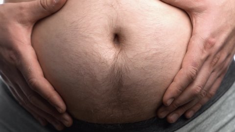 Fat man with a big belly shows his fat on a white screen. Male stomach, overweight.