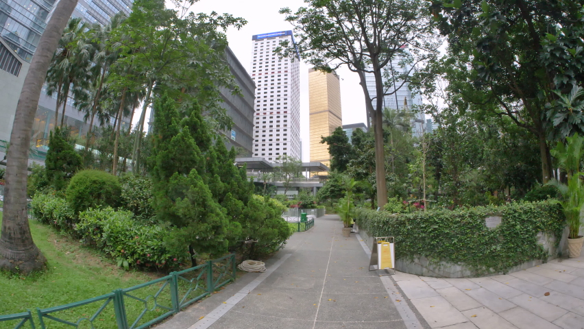 Beautiful city park in the city center of Hong Kong. China. Fontaine. China City. Green park. People chilling in the square. Young European Woman is sitting on a bench, surfing on Cell phone. Dolly in
