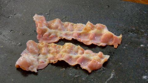 Close-up of bacon strips flipped with a spatula on the flat grill surface outdoors