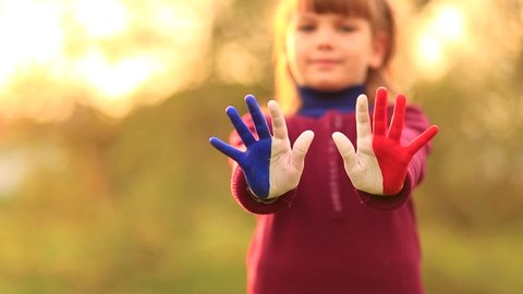 Joyful girl waving hands painted in France flag colors and say hello outdoor at sunset background