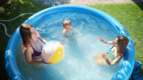 Slow motion of happy cheerful family having fun with inflatable beach ball in outdoor swimming pool. Concept of happy and cheerful summer holidays and vacation.