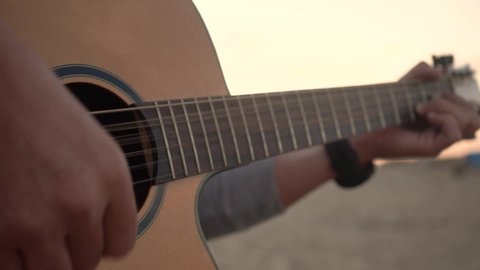Close up shot of a boy who plays guitar by the beach during sunset.