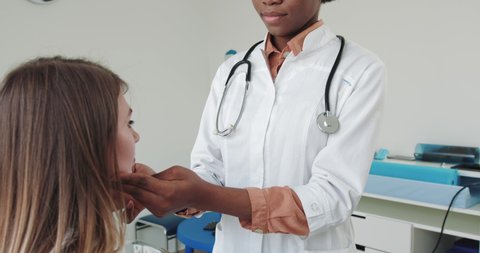 Endocrinologist Examining Patient's Thyroid Gland, Iodine Deficiency Symptom Female Doctor Checking Thyroid Gland Of Girl Patient Touching Neck. Young Girl At A Reception At An African-American Doctor
