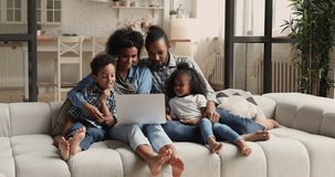 Young African couple little adorable kids relaxing on couch with laptop, family watch funny cartoons, comedy movie laughing feels happy and carefree. Weekend using wireless tech and on-line tv concept