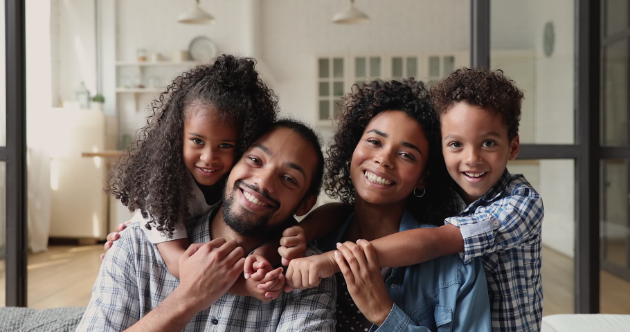 Young african couple with little kids sit on couch, cute children piggyback embrace loving parents smile look at camera. Medical insurance cover or full family, new house and happy homeowners concept | Shutterstock HD Video #1065626641