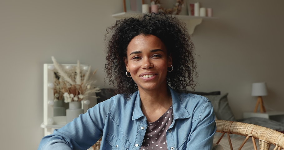Smiling positive african woman sit indoor looking at camera talking using video call. Video conferencing with family or friend remotely through web chat, modern tech and pleasant conversation concept Royalty-Free Stock Footage #1065626665