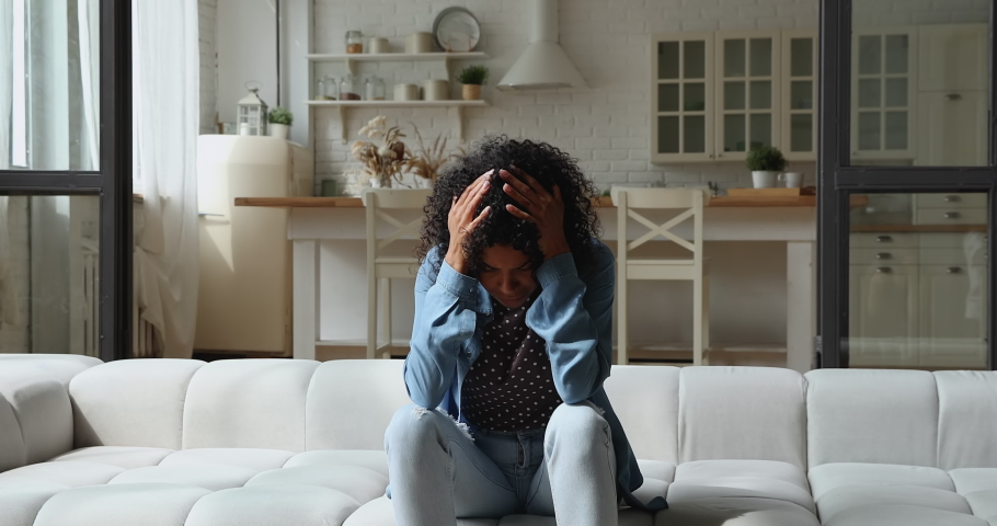 Stressed single african female sit on sofa covers ears with hands having headache feels annoyed about too noisy kids playing running at home. Upbringing difficulties, divorced depressed parent concept Royalty-Free Stock Footage #1065627481