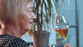 Evening party with alcohol beverage. Portrait of the beautiful senior blonde lady drinking alcohol and enjoying smell of white wine while sitting at the bartender. Elderly people concept. Stock video
