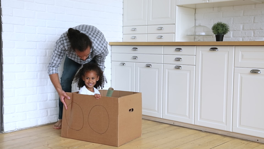 Slow motion African father riding little adorable 4s daughter while she sitting inside of cardboard box, active family play games at modern warm kitchen, celebrate relocation day to new home concept Royalty-Free Stock Footage #1065628672