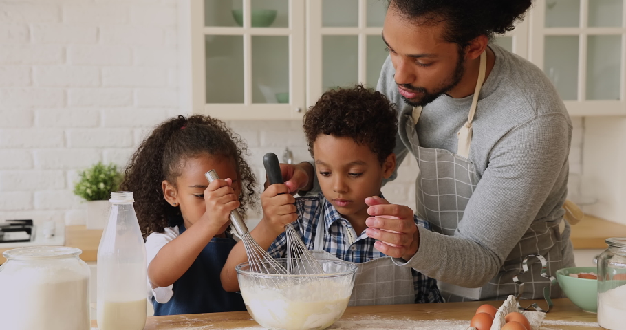 African dad and kids cooking together in kitchen, prepare whisk mixture for dough, father add milk help teach spend time with pretty siblings. Develop children, make surprise, holiday dinner concept Royalty-Free Stock Footage #1065628699