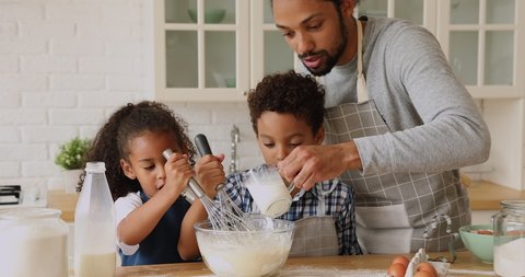 African dad and kids cooking together in kitchen, prepare whisk mixture for dough, father add milk help teach spend time with pretty siblings. Develop children, make surprise, holiday dinner concept