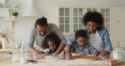 African couple with small 5s adorable kids preparing dough for cookies, happy family roll out dough with rolling pin enjoy process spend weekend together. Develop children, parenthood, cookery concept