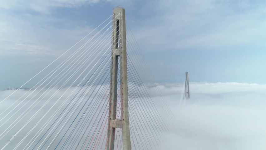 Aerial epic around fog-covered pylons guy of modern Russian bridge Cinematic Vladivostok cloudy weather condition. Far East epic downtown. Travel attraction. Open space. Simbol of city Professional 4k