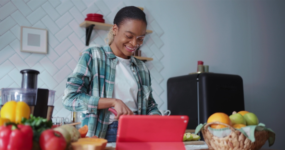 Afro-american attractive woman using digital tablet videochatting with family while cooking healthy breakfast in home kitchen. Online communication. Royalty-Free Stock Footage #1065636070