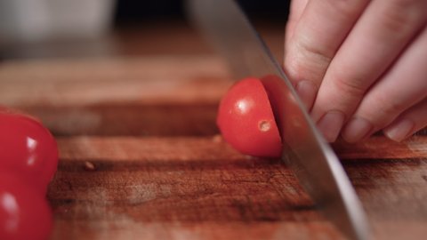 Slicing cherry tomatoes with a knife. Closeup chef cuts vegetables on wooden board