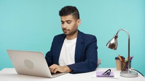 Self confident successful businessman showing his strength and independence looking at web camera of his laptop, bragging his leadership qualities. Indoor studio shot isolated on blue background