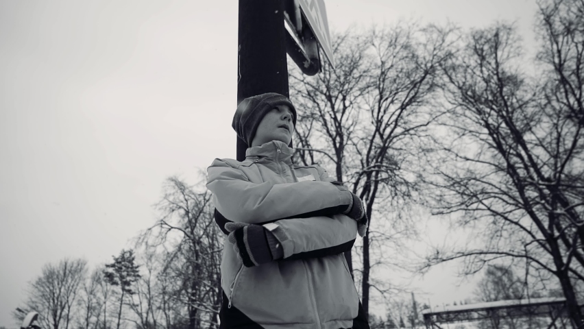 A cool boy stands near a metal pole under the falling snow. Taken with a wide-angle lens