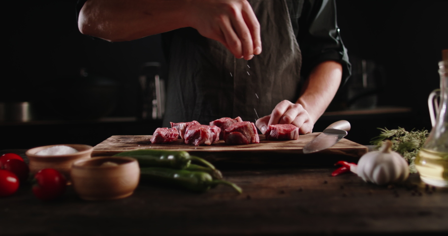 Chef cooks beef steak, sprinkling with salt on a background of professional kitchen, slow motion. | Shutterstock HD Video #1065641494