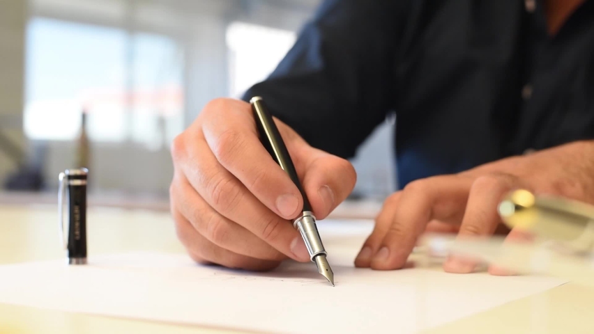 The hand of a man making a signature with his fountain pen. Silver fountain pen with black details. Businessman signing documents. A businessman signing documents with a fountain pen Royalty-Free Stock Footage #1065652531