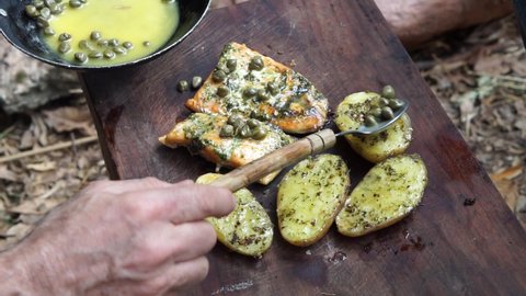 Putting melted butter with caper on the grilled salmon and rustic potatoes