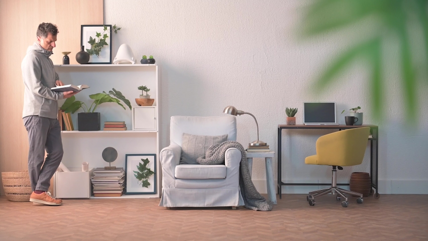 Adult man read a book, bookshelf, sofa and working table style. Spend a good time at home.