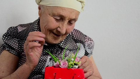 Happy grandmother with a gift. Gift and flowers in mother's old wrinkled hands. International Women's Day. The concept of the holiday and congratulations. March 8. Mothers Day.Grandma accepts a gift
