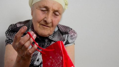  International Women's Day. Congratulations concept. Old grandmother with a gift in her hands.The old grandmother opens the gift. Happy grandmother with a smile examines a gift for Mother's Day.