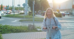 Happy blonde woman rides scooter around the city at sunset. Move even faster thanks to scooters. 4K video Slow motion.