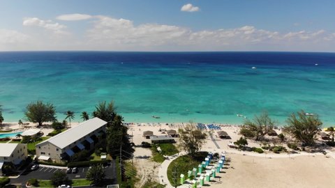 aerial footage of seven mile beach on grand cayman in the cayman islands showing bright golden sand and crystal clear turquoise and deep blue and green waters in the caribbean sea on a summer day.