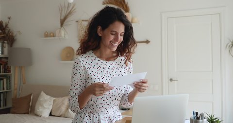 Happy attractive young woman opening paper envelope, reading pleasant news in letter postal correspondence, feeling excited of getting event invitation or university admission post notification.
