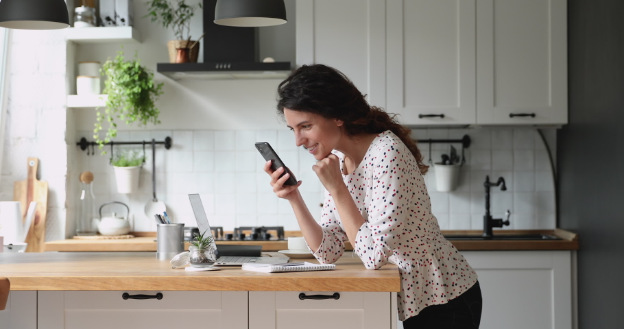 Addicted to social networks young happy beautiful woman scrolling profile pages, zooming photos, reading friends life news feed posts using mobile phone application, standing in modern kitchen alone. | Shutterstock HD Video #1065667522