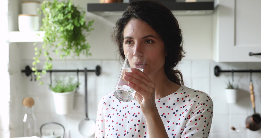 Head shot beautiful young dreamy caucasian woman drinking glass of fresh pure water, enjoying healthy morning habit alone in modern kitchen, starting new energetic day, feeling refreshed and hydrated. Royalty-Free Stock Footage #1065667666