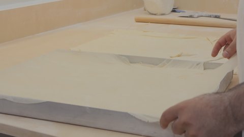 the baker places ultra-thin layers of dough on a baking sheet to prepare a baklava.