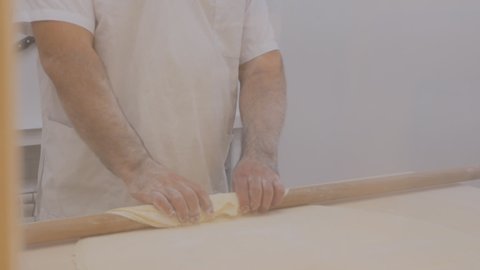 a male baker of Kurdish nationality works with puff pastry. The baker takes a long rolling pin from the wall and rolls out the dough. Close-up. Cooking Turkish baklava