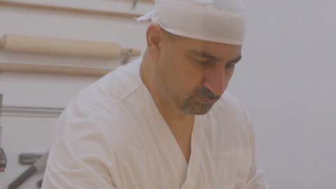 baker male Kurd prepares puff pastry for Turkish baklava. The baker is dressed in white clothes and a hat. The pastry chef works behind the glass.