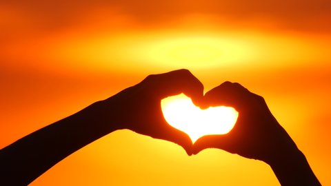 Silhouette hands up showing sign heart a symbol love or feeling. Feel good making hands in heart in romantic travel. Love sign or gesture at sunset and sun light through heart made by hand in vacation