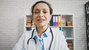 Professional female doctor in uniform with stethoscope sitting at office and talking to camera. Physician blogger teaching healthcare rules online, conference video call. Medical video blog. Close up