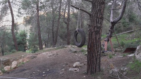 Car tire swings on the wind in the forest. Not finished house on the tree in the background