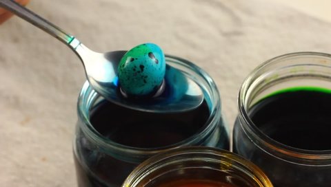 A child of Caucasian nationality paints small clouds of quail eggs with a metal spoon and lowers them into a glass jar with dyes on the Easter table. Concept for spring religious holidays