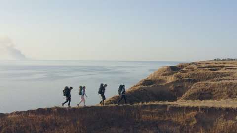 The four people with backpacks walking in the mountains against the seascape 스톡 비디오