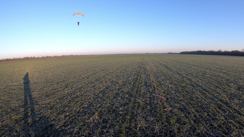 Parachutist wearing special protective equipment lands enjoying paragliding and runs along field giving high five close view
