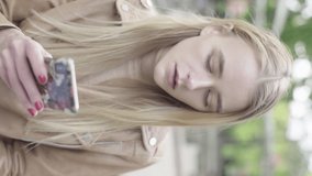 Vertical video of a young skinny girl in the park. Girl with a mobile phone.