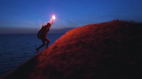The man with a fire stick climbing the mountain near the sea. slow motion