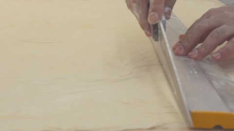 the baker cuts the dough with a knife in a straight line. A man pastry chef using a metal ruler and a knife cuts the dough for Turkish baklava