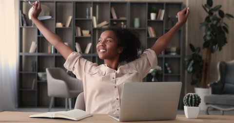 Smiling african businesswoman or student finished computer work, take off glasses stretching relaxing seated at workplace feeling stress relief, satisfied by project accomplishment, task done in time