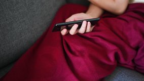 Woman using phone while lying down on sofa closeup.
