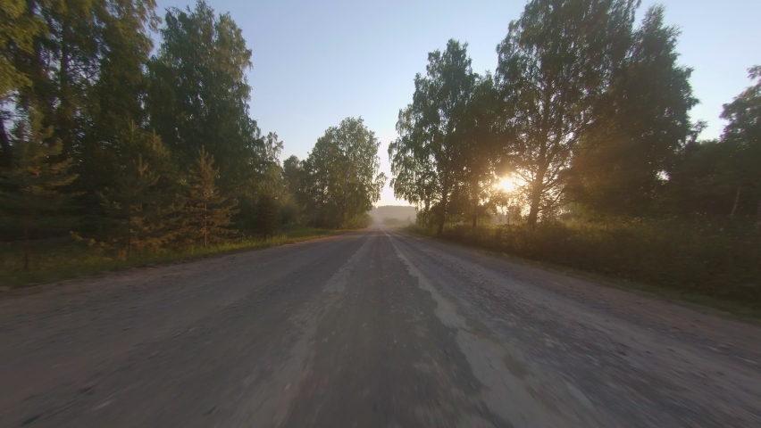 Car driving fast on a scenic road around trees at summer sunrise. Point of view footage while driving down a road in rural. Travel concept. 