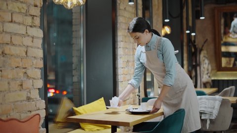 Young waitress clearing the table in cafe, working in coffee shop, service