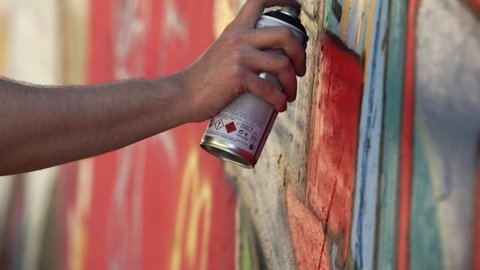 A graffiti artist paints a wall with spraycan. Close up image of man's hands while painting. Urban culture, creativity, street art concept.